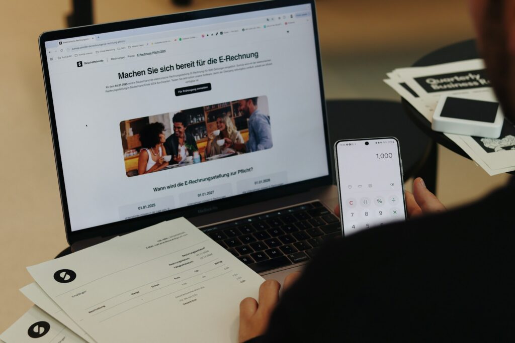 Laptop und Smartphone zeigen Hinweis zur E-Rechnungspflicht neben Rechnungsunterlagen auf dem Schreibtisch